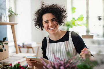 Portrait of happy young woman with clipboard in a small shop with plants