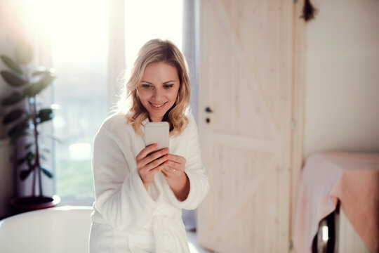 Smiling woman wearing bathrobe in bathroom at home holding cell phone