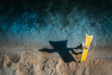 Girl with wooly hat, standing at lakeshore, carrying airbed