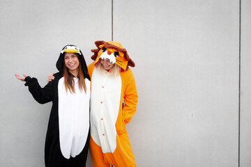 Two women in penguin and lion costume in front of concrete wall