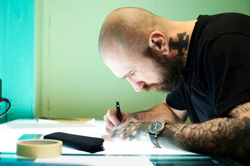 Tattoo artist designing motif on light table in studio
