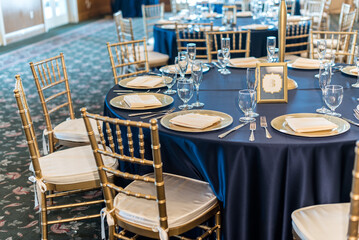 Tables are elegantly set with plates and silverware in a dining hall for a wedding reception