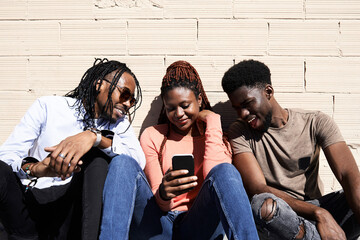 Three friends sitting together and watching a video on a smartphone outdoors