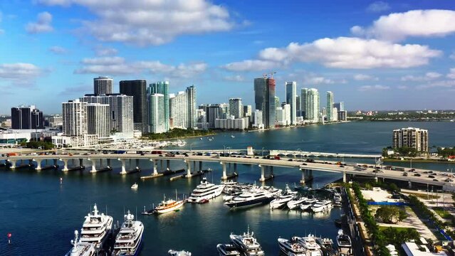 4k Aerial footage stunning aerial view of Miamis skyline with highrise buildings, a highway, busy marina, and luxurious yachts on a sunny day, showcasing the vibrant city life and modern architecture
