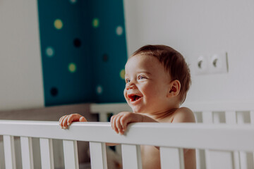 Baby boy standing in his cot, laughing © tunedin