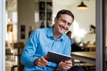 Smiling businessman with tablet sitting at open French door