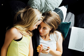 Relaxed mother and daughter with cell phone on sofa