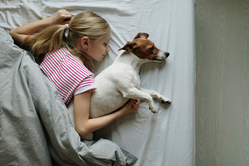 Blond girl lying on bed with her dog sleeping, top view