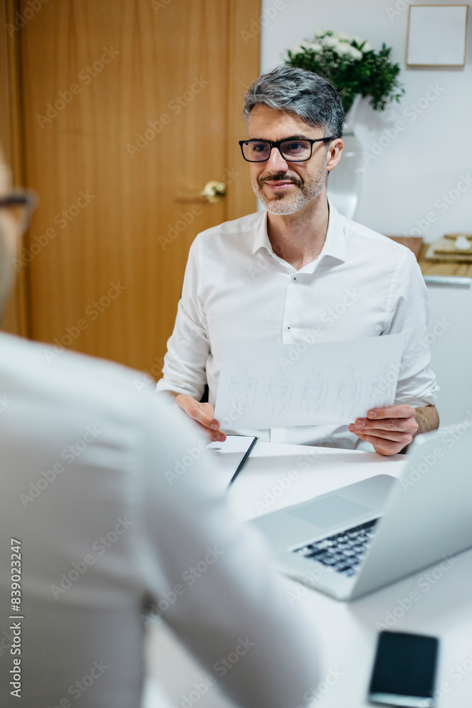 Poster Smiling man at desk holding paper looking at colleague