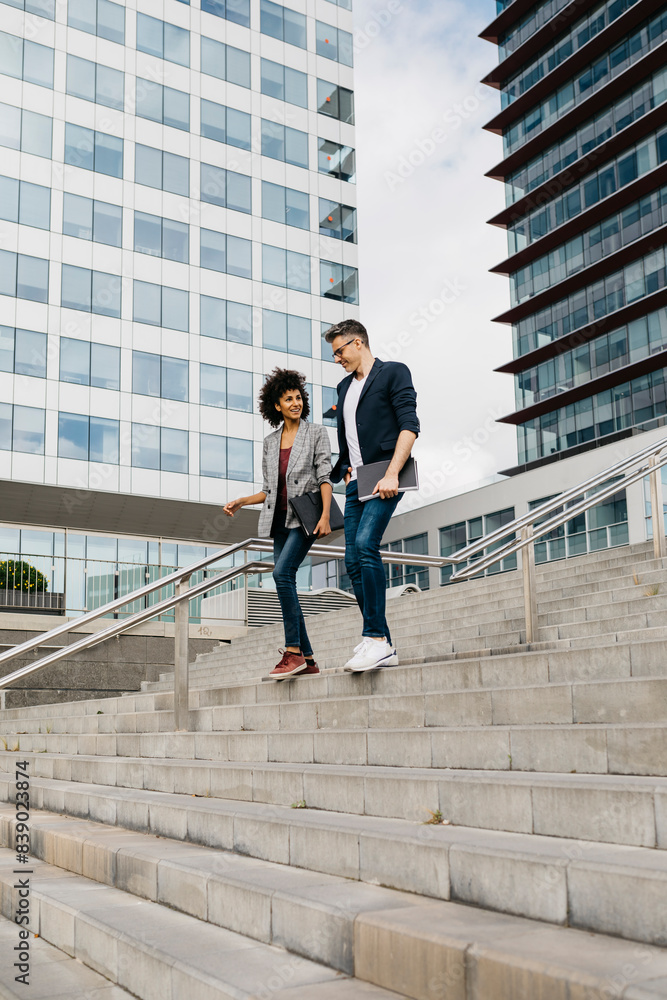 Poster two colleagues walking and talking on stairs outside office building in the city