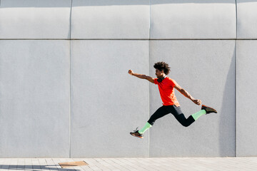 Young man doing jumps with a gray wall in the background