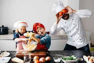 Playful father with two kids covering his eyes with tomatoes in kitchen
