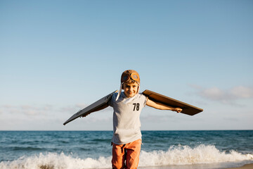 Boy wearing aviator's cap and cardboard wings at beach