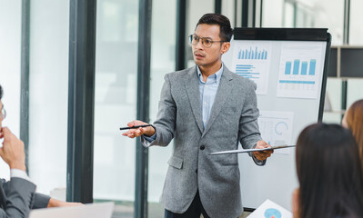 Businessman in a grey suit leads a presentation with charts and graphs in a modern office.