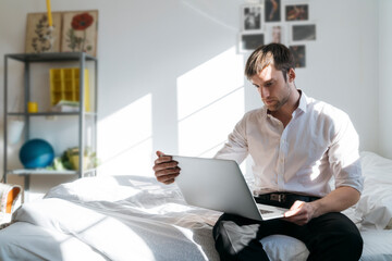 Young man sitting on bed using laptop