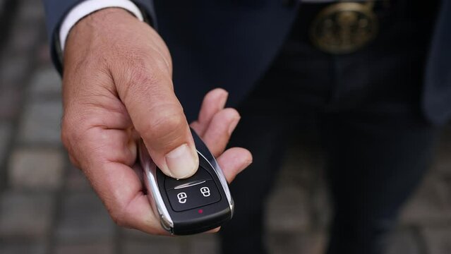 Unlocking the car using the car key fob. A close-up view of the car's owner pressing a button on the remote.