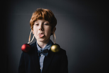Portrait of redheaded boy wearing bow tie and Christmas baubles sticking out tongue
