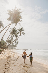 Full length of couple walking on beach against sky during sunny day, Sri Lanka