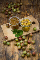 Jar of gooseberry jam, gooseberries and glass of preserved gooseberries on wooden board