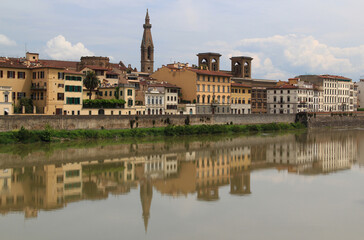 Obraz premium Cityscape view of the Arno river embankment with buildings reflected in it against a blue sky with clouds in the city of Florence, Italy