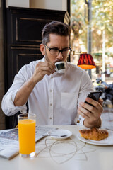 Businessman having breakfast in a cafe and checking cell phone