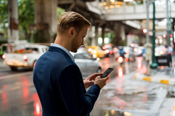 Young businessman using smartphone in Bangkok during a rainy day