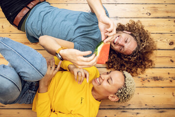 Happy young couple lying on the floor at home sharing a watermelon