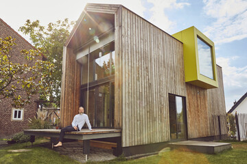 Mature man with beer bottle sitting outside tiny house during summer