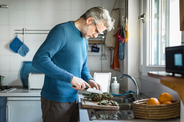 Mature man preparing artichokes in his kitchen