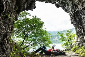 Mature man reading book while lying at cave entrance by Lake Como