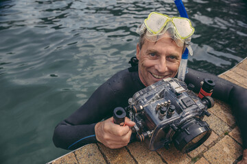 Portrait of happy man with underwater DSLR camera case in water