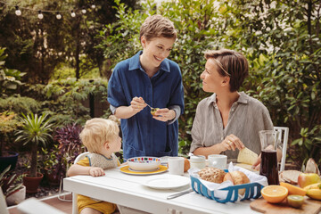 Two happy mothers at breakfast table outdoors with their child