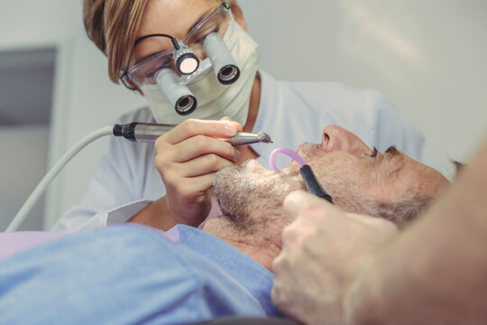 Patient getting dental treatment, dentist using dental drill and head magnifiers and light