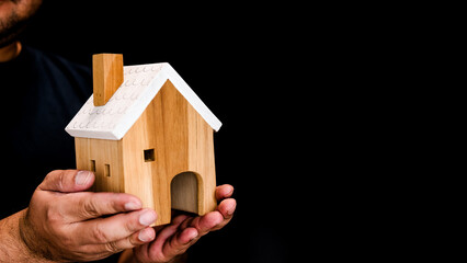 Wooden house on a man hand on a black background. The concept of family happiness, buying a house....