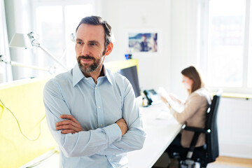 Portrait of confident businessman in office with employee in background