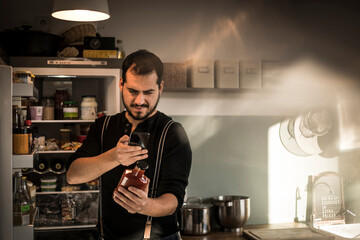 Man standing in front of fridge, scanning sauce bottle with his smartphone