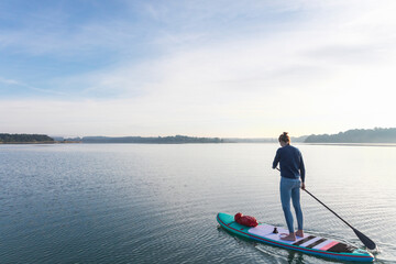 Woman standing on sup board in the morning on a lake