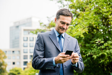 Businessman using cell phone in city park