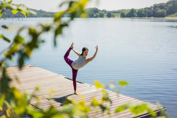 Mature woman practicing yoga in summer on a jetty at a lake