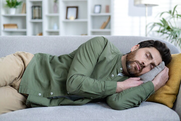 Man taking a nap on a comfortable couch in a well-lit living room. Relaxation and rest in a cozy home environment.