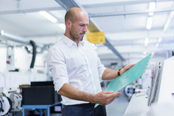 Confident mature male engineer analyzing large circuit board at illuminated factory
