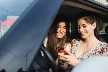 Two happy young women looking at cell phone in a car