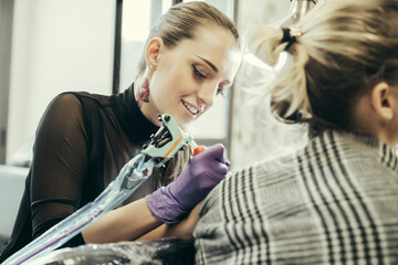 female tattooist tattooing upper arm of female customer