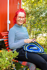 Portrait of smiling senior woman with red dyed hair sitting in front of red trailer in the garden...