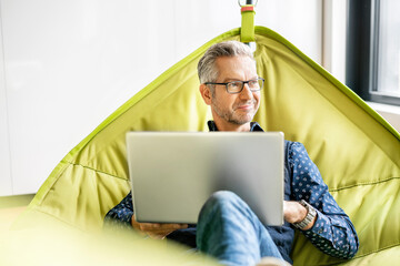 Smiling businessman sitting in hammock, using laptop