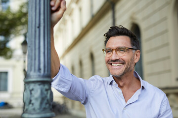 Portrait of happy businessman leaning against lamp post in the city