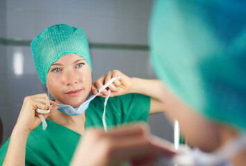 Woman in scrubs looking in mirror putting on mask