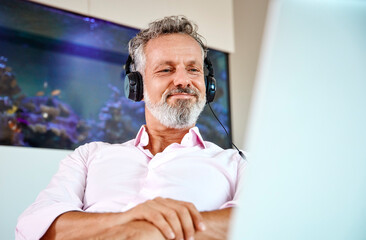 Businessman with headphones using laptop at desk in front of aquarium
