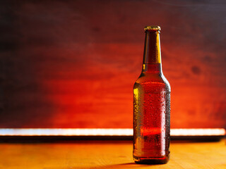 Cold beer bottle in drops on a wooden background, copy space. Back light