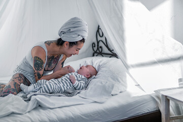 Tattooed young woman with her baby in canopy bed
